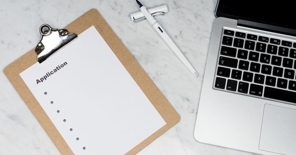 Application form on a clipboard beside a pen and laptop on a desk